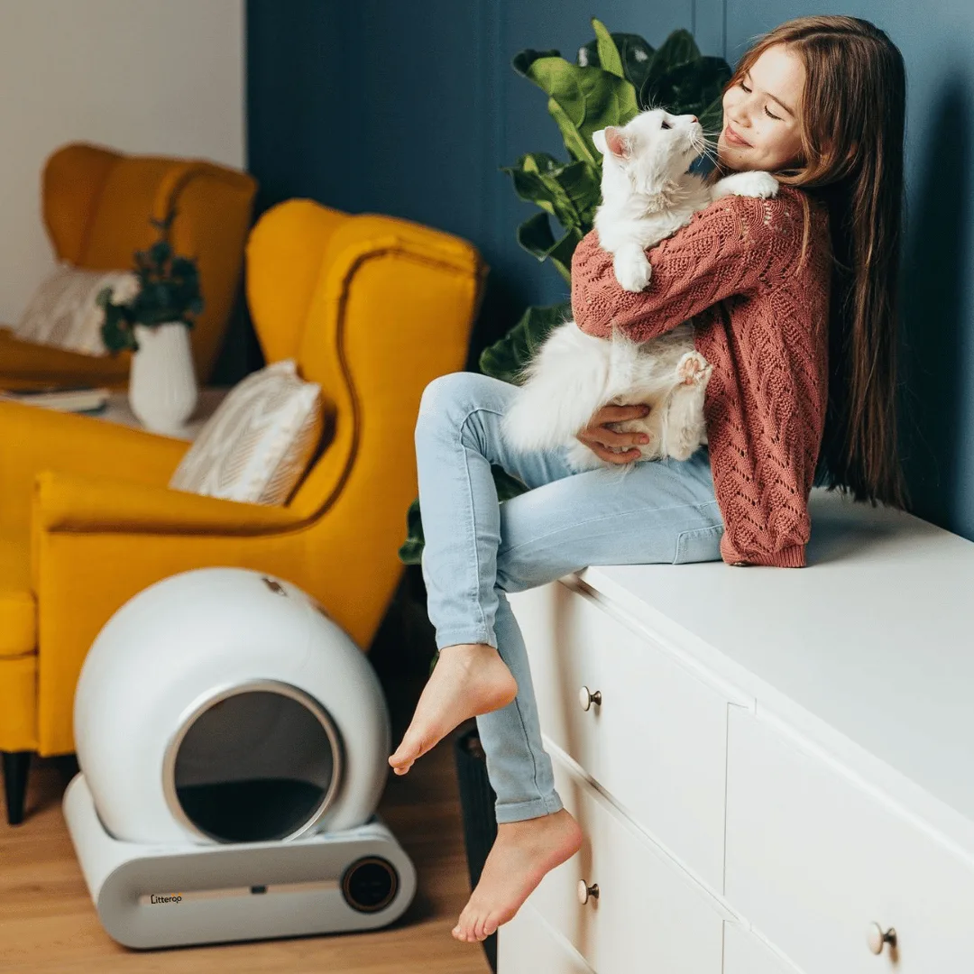 Een vrouw met haar kat op een gele fauteuil, met de Litteroo One ernaast